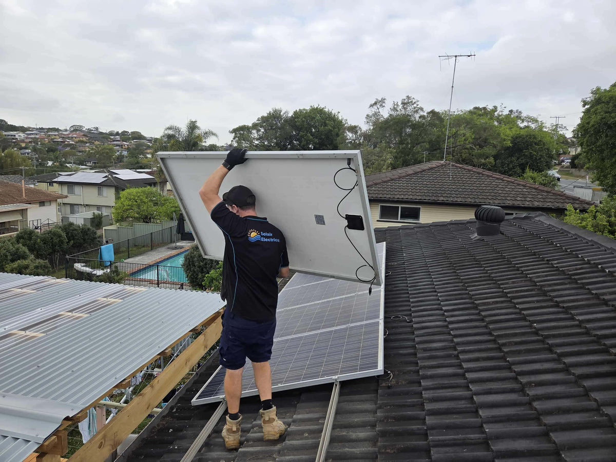 Worker holding a solar panel above a tiled roof